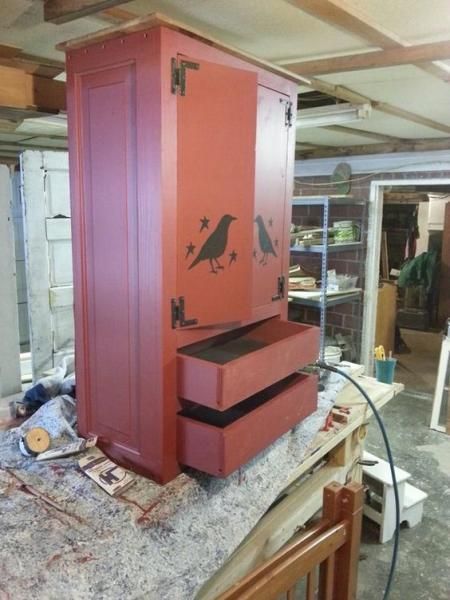 Red wooden cabinet with drawers and bird stencils on a workbench in a workshop