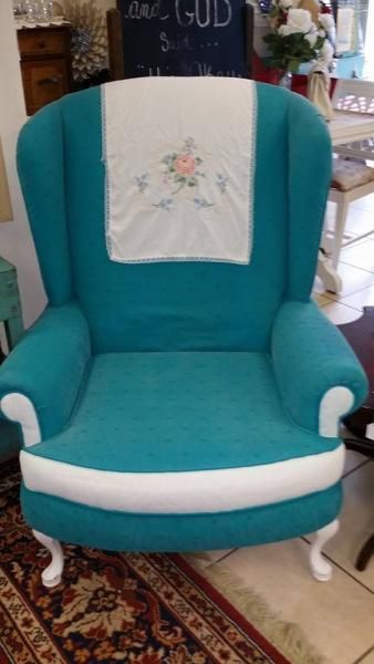 Teal upholstered armchair with white trim and a floral embroidered cloth draped over the back.