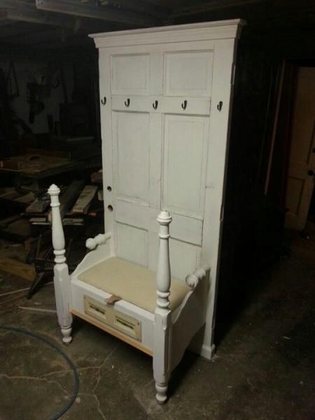 White wooden wardrobe with bench seat and turned posts in a dim workshop, viewed from the front.