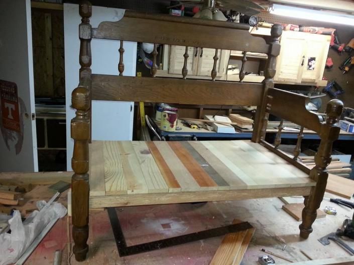 Wooden rocking cradle frame under construction in a workshop, with unfinished planks and tools nearby