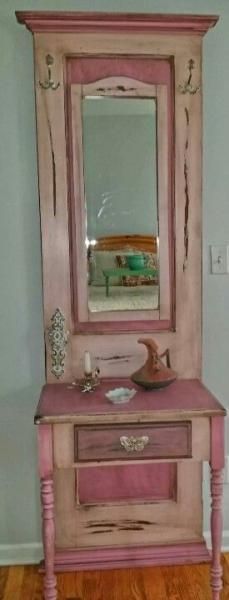 Pink vintage vanity with mirror and small items on top against a wall.