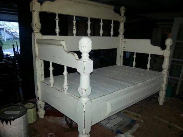 White wooden bed frame with turned posts in a dim room, viewed from the side.