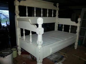 White wooden bed frame with turned posts and slatted base in a dim workshop or garage setting