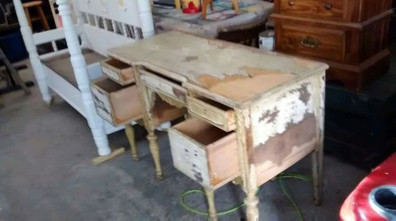 Worn wooden desk and matching chair in a garage, with peeling white paint and a small drawer unit.
