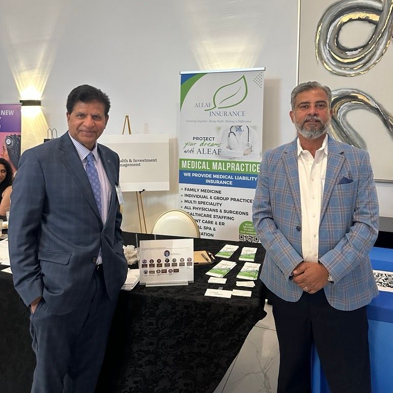 Two men at a trade show booth. One in a suit, the other in a blazer, pose by a medical malpractice insurance sign.