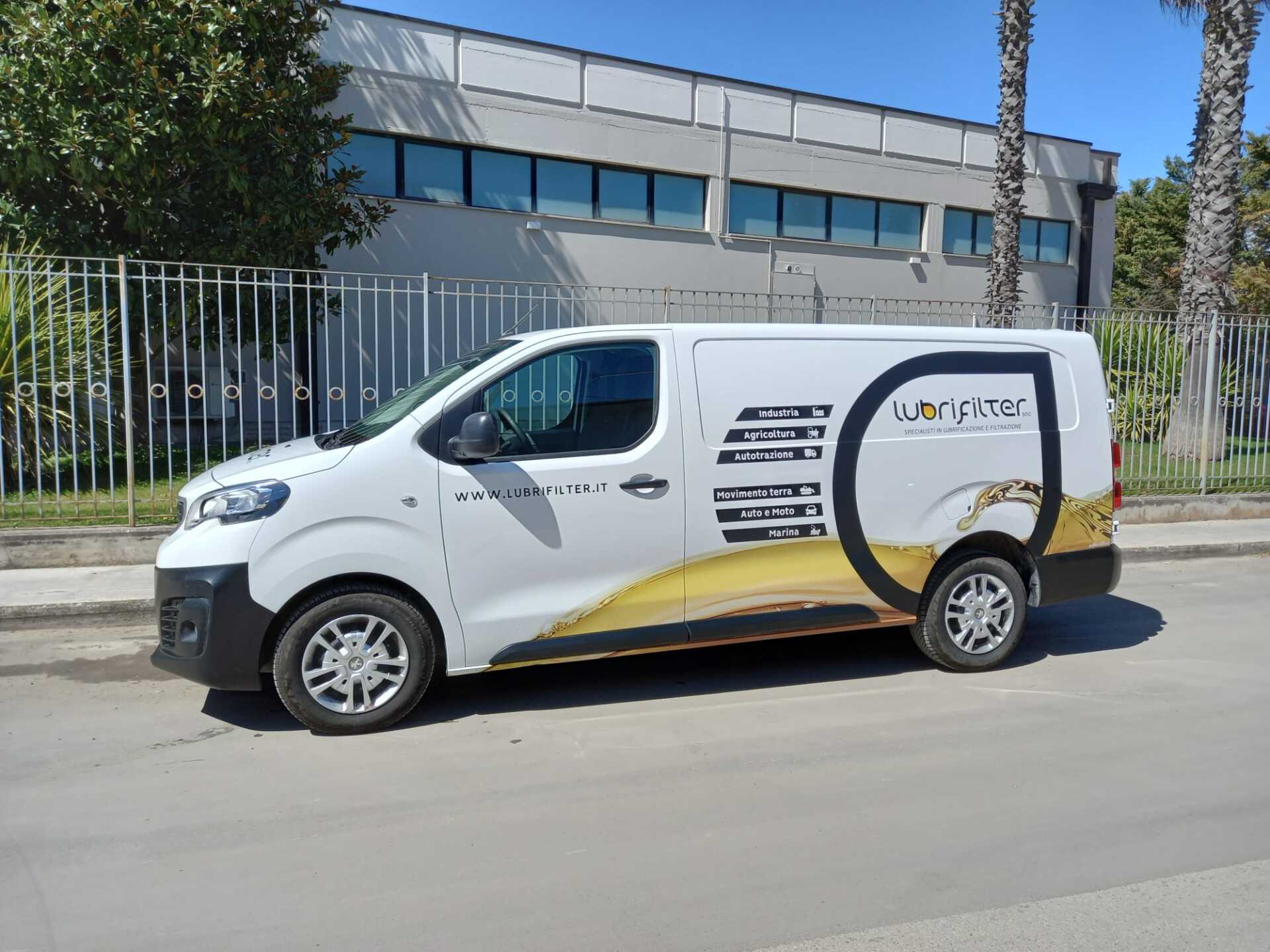 Furgone bianco con grafica dorata parcheggiato sulla strada di fronte a un edificio.