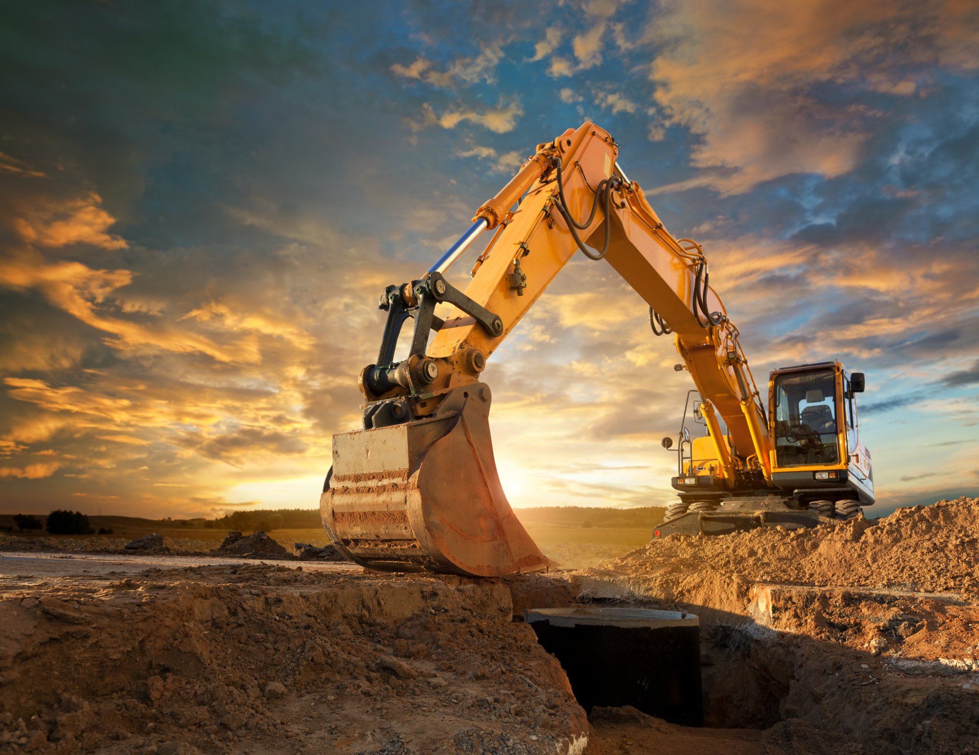 Escavatore giallo che scava in un cantiere al tramonto.