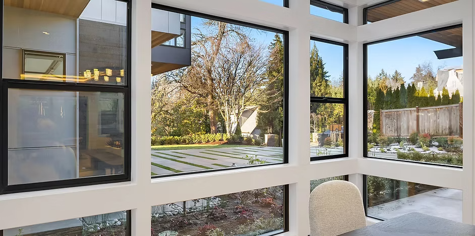 A modern room with large windows offering a view of a backyard, trees, and an adjacent building.