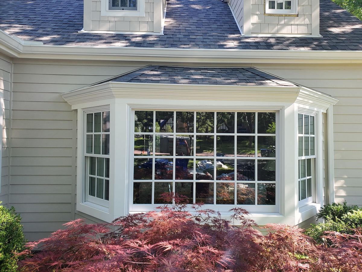 Bay window on a light-colored house with white trim. A red bush is in front.