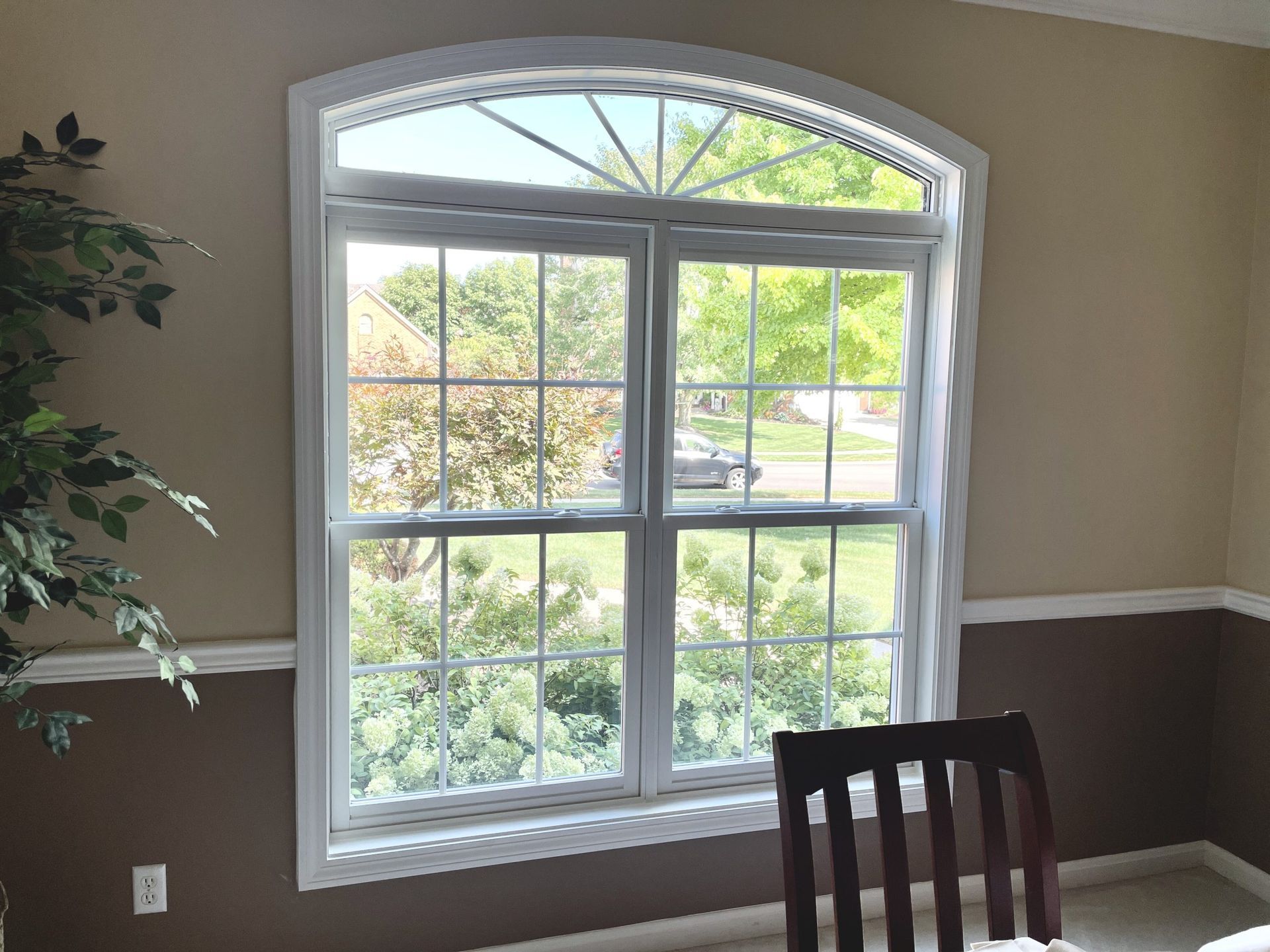 Arched window with white trim; inside view, trees and sky seen through glass. White molding against tan and brown walls.