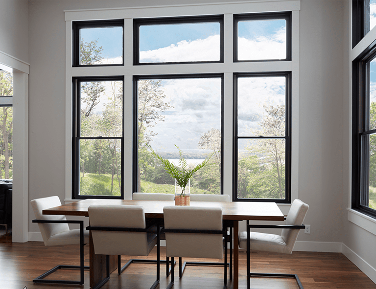 Dining room with large windows overlooking a scenic view; a wooden table and modern chairs are visible.