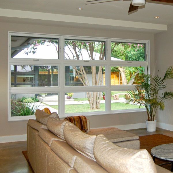 Living room with large window overlooking a yard, tan couch, potted plant, and coffee table.