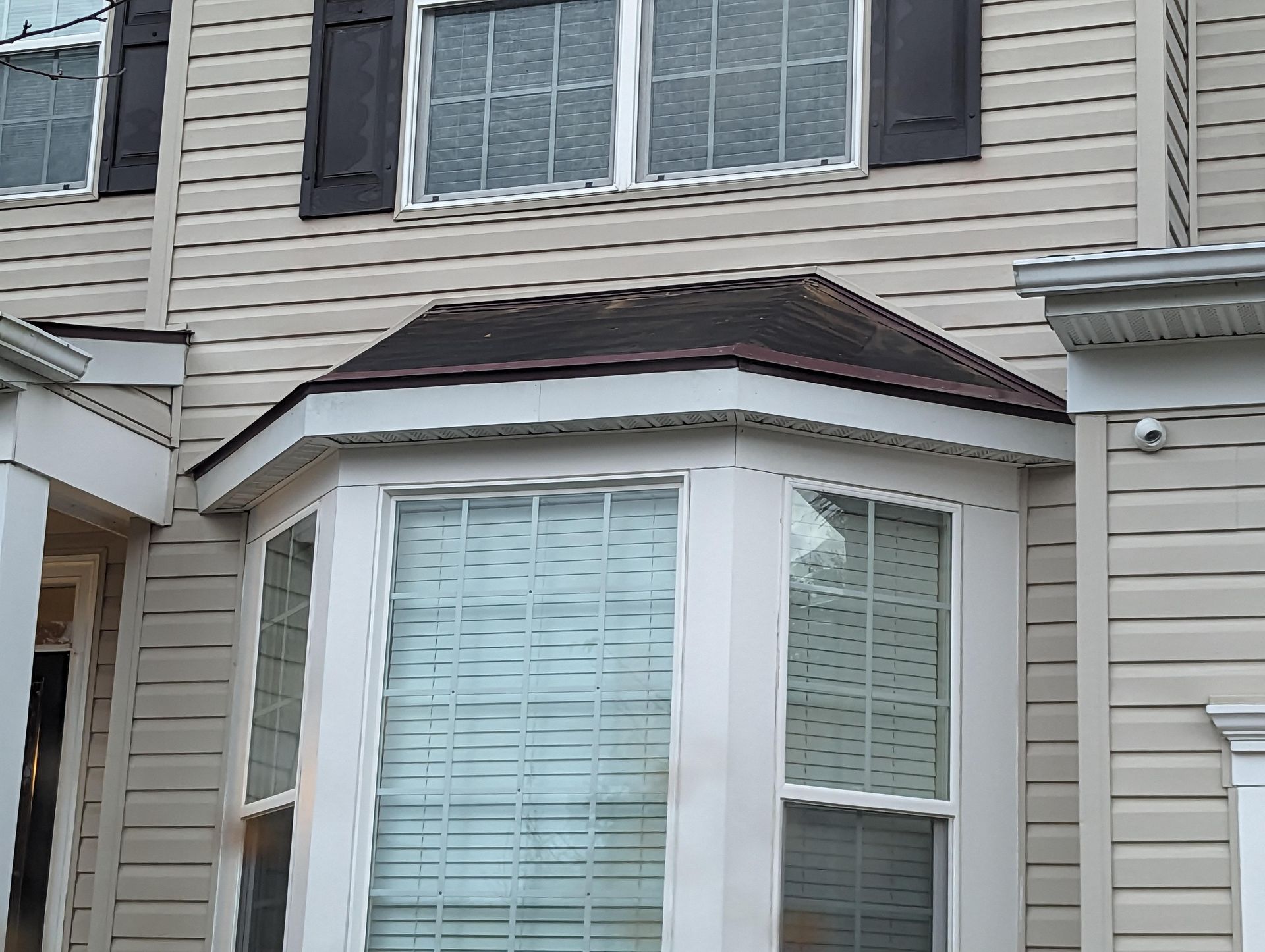 Close-up of a beige two-story house with bay windows and dark shutters.