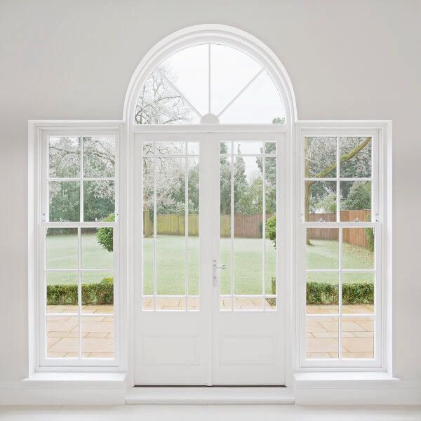 White double doors and windows with arched top, overlooking a garden.
