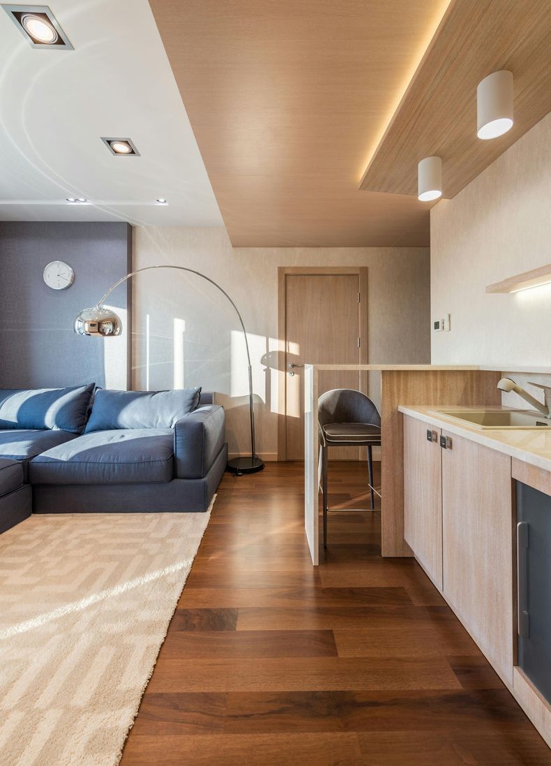 Modern living room with wood floors, blue couch, kitchen bar.