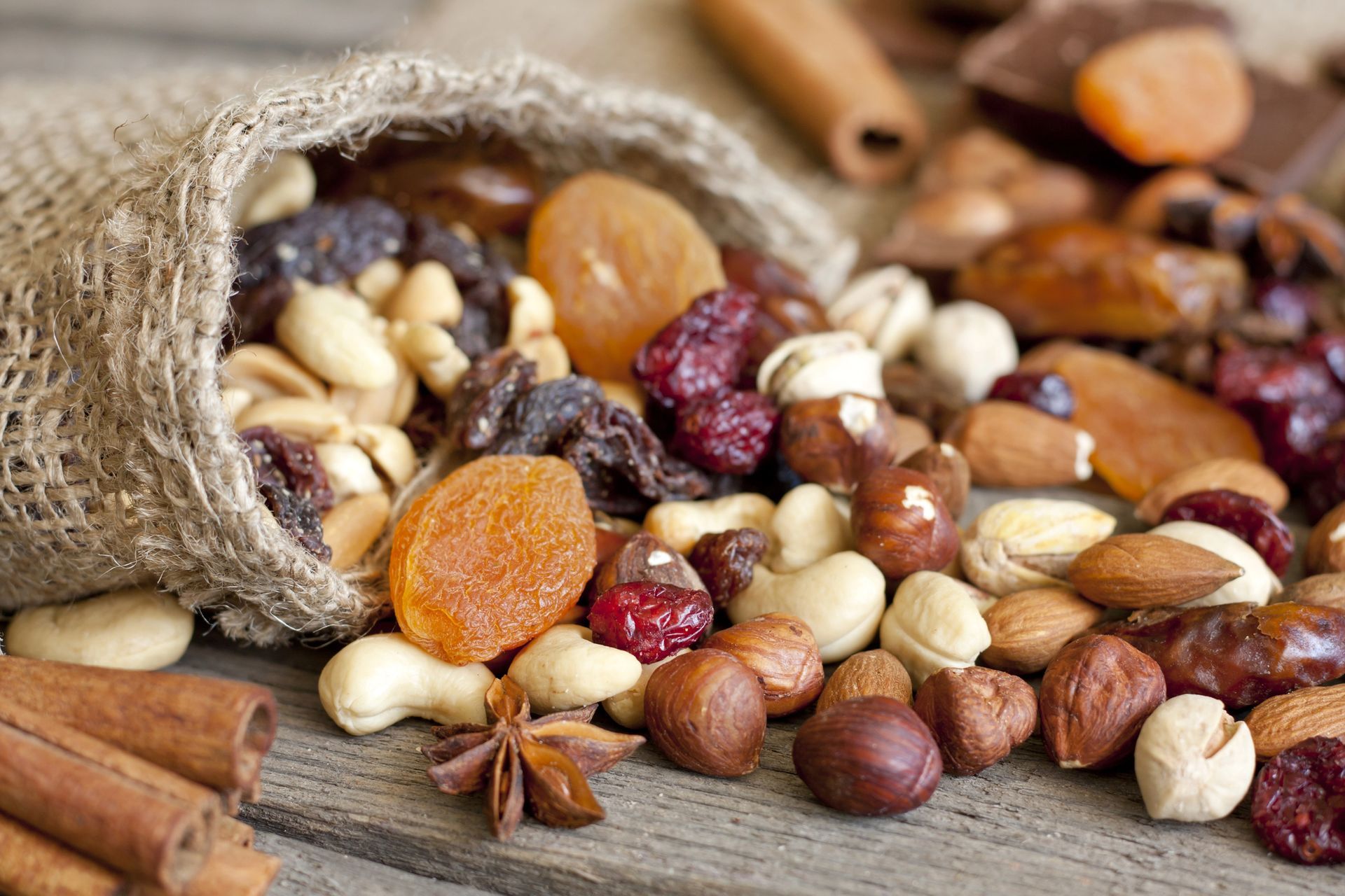Frutos secos, frutas secas y especias derramándose desde una bolsa de arpillera sobre una superficie de madera.