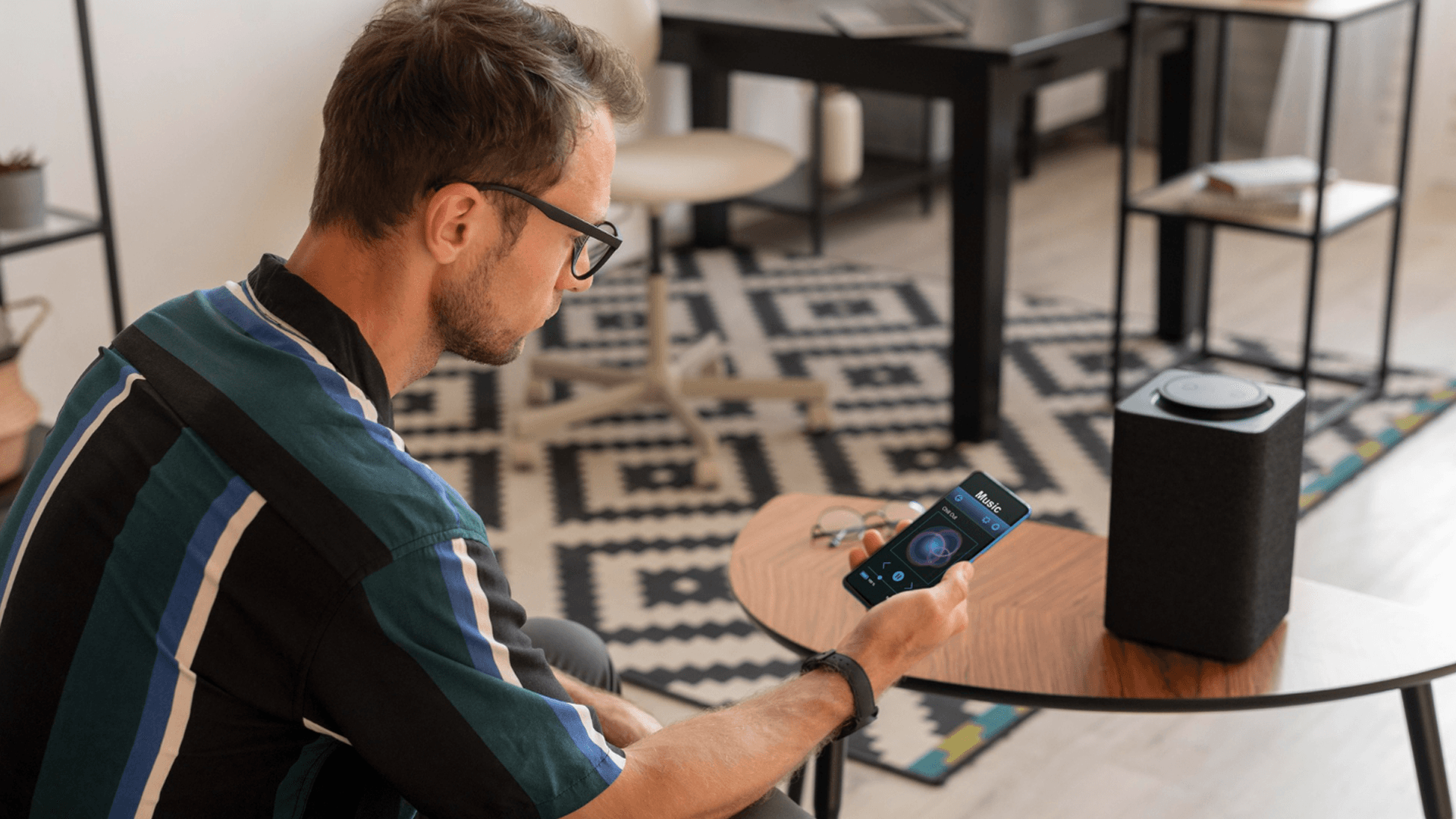 Um homem está sentado no chão de uma sala usando um smartphone.