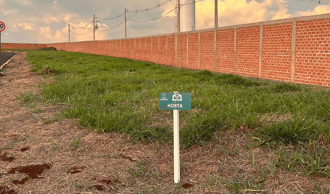 Uma placa está no meio de um campo gramado próximo a uma parede de tijolos.