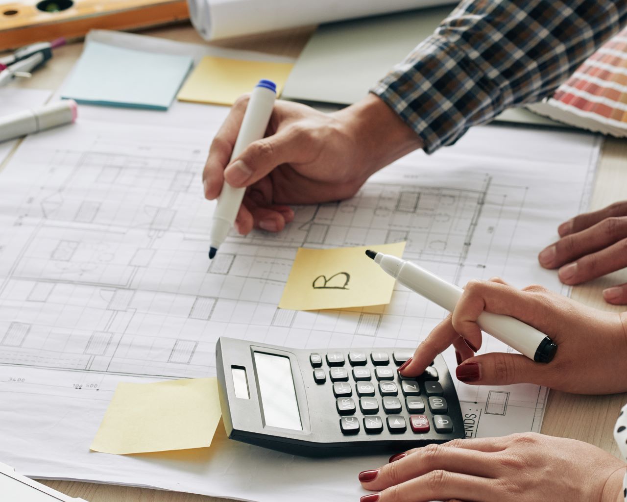 calculando-projetos-de-arquitetura Um homem está usando uma calculadora enquanto uma mulher escreve em um post-it.