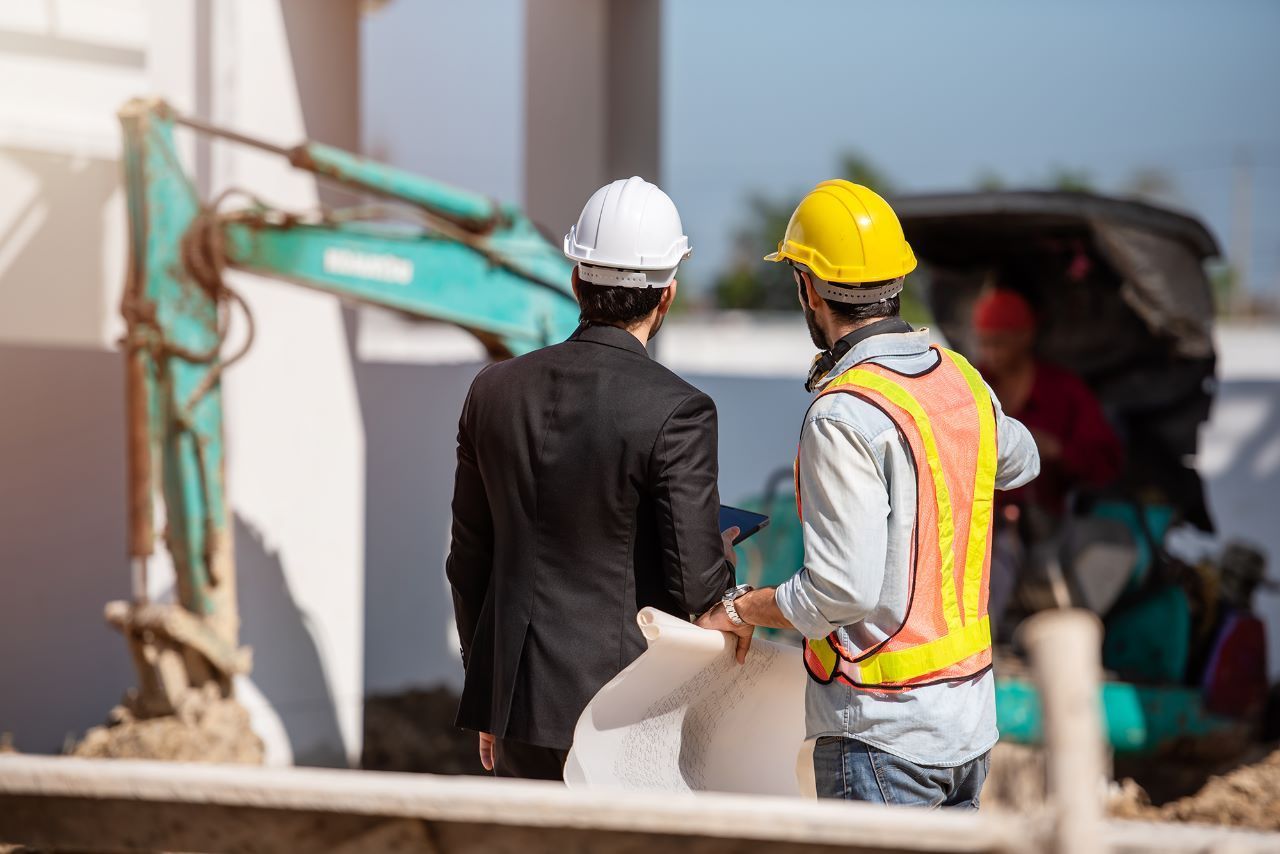engenheiro-em-obra Dois trabalhadores da construção civil estão próximos um do outro em um canteiro de obras.