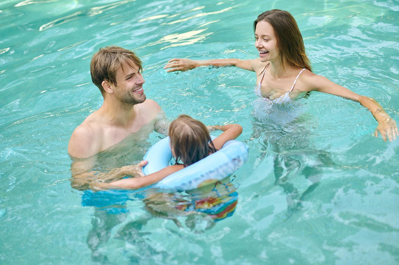 familia-na-piscina-condominio-fechado Um homem, uma mulher e uma criança brincam numa piscina.