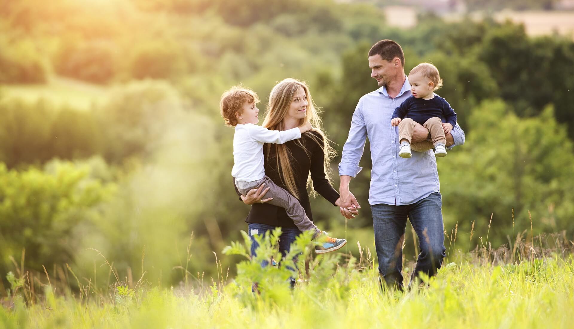 familia-no-campo Uma família caminha de mãos dadas por um campo gramado.