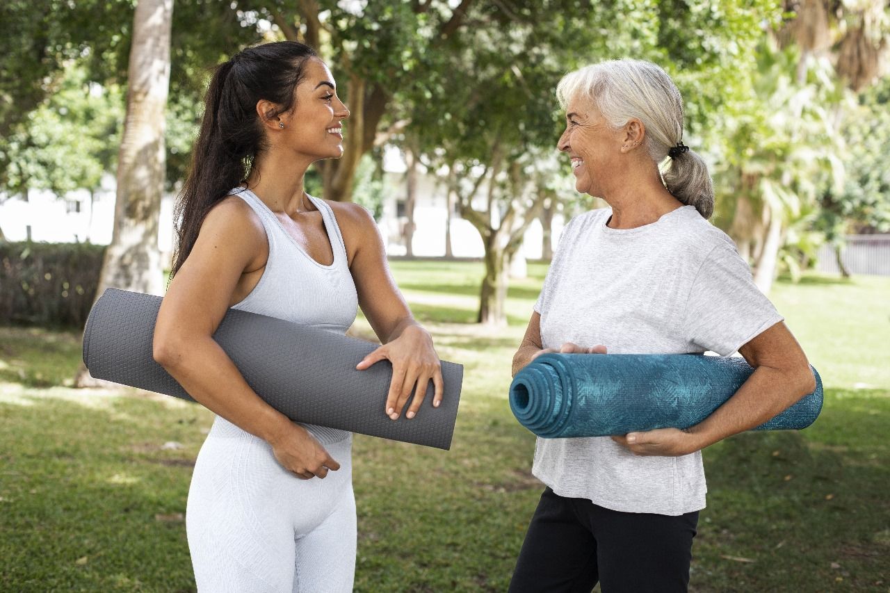 mulheres-treinando-em-ourinhos Duas mulheres estão segurando tapetes de ioga em um parque e conversando entre si.