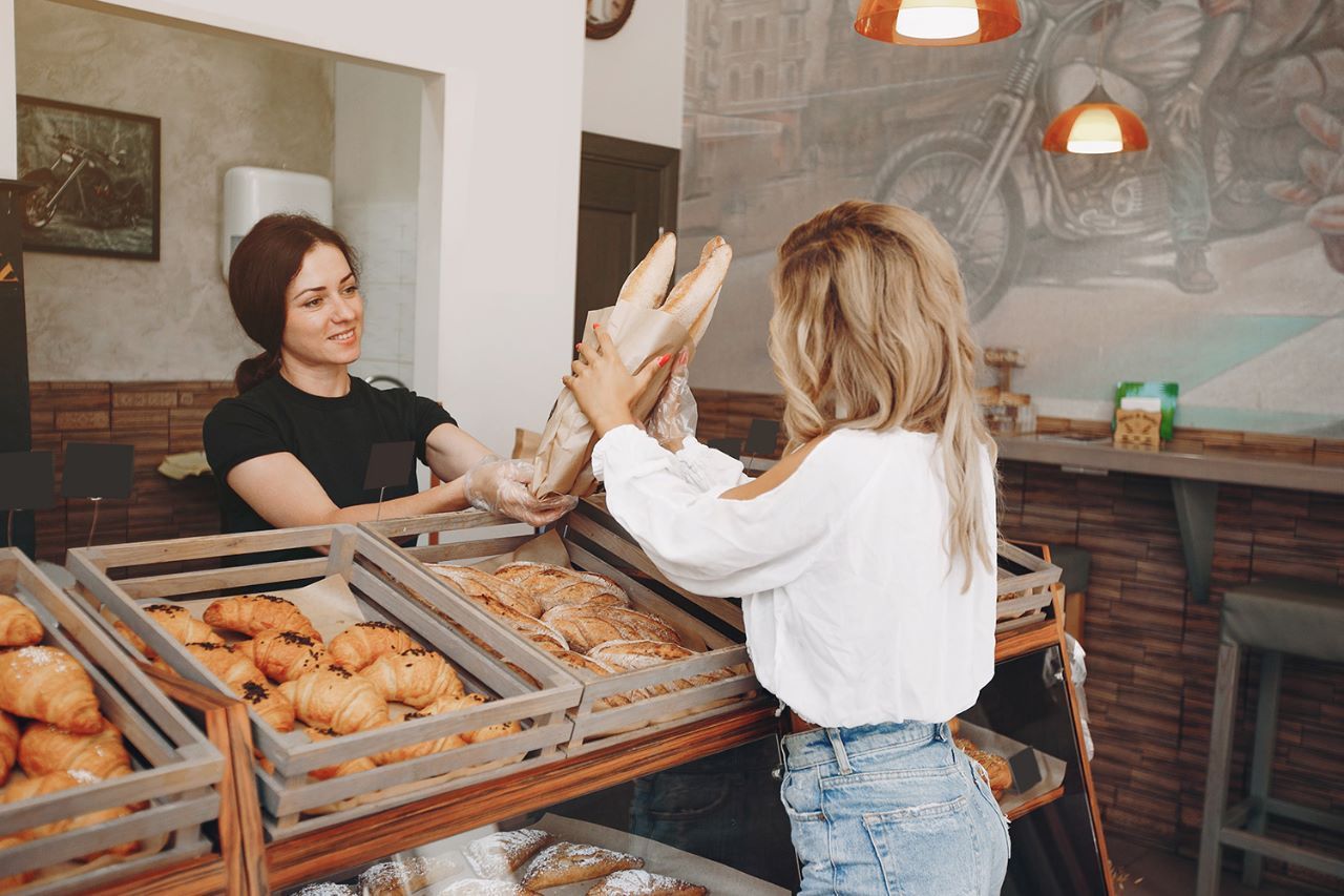 Uma mulher está dando um pão a uma criança em uma padaria.