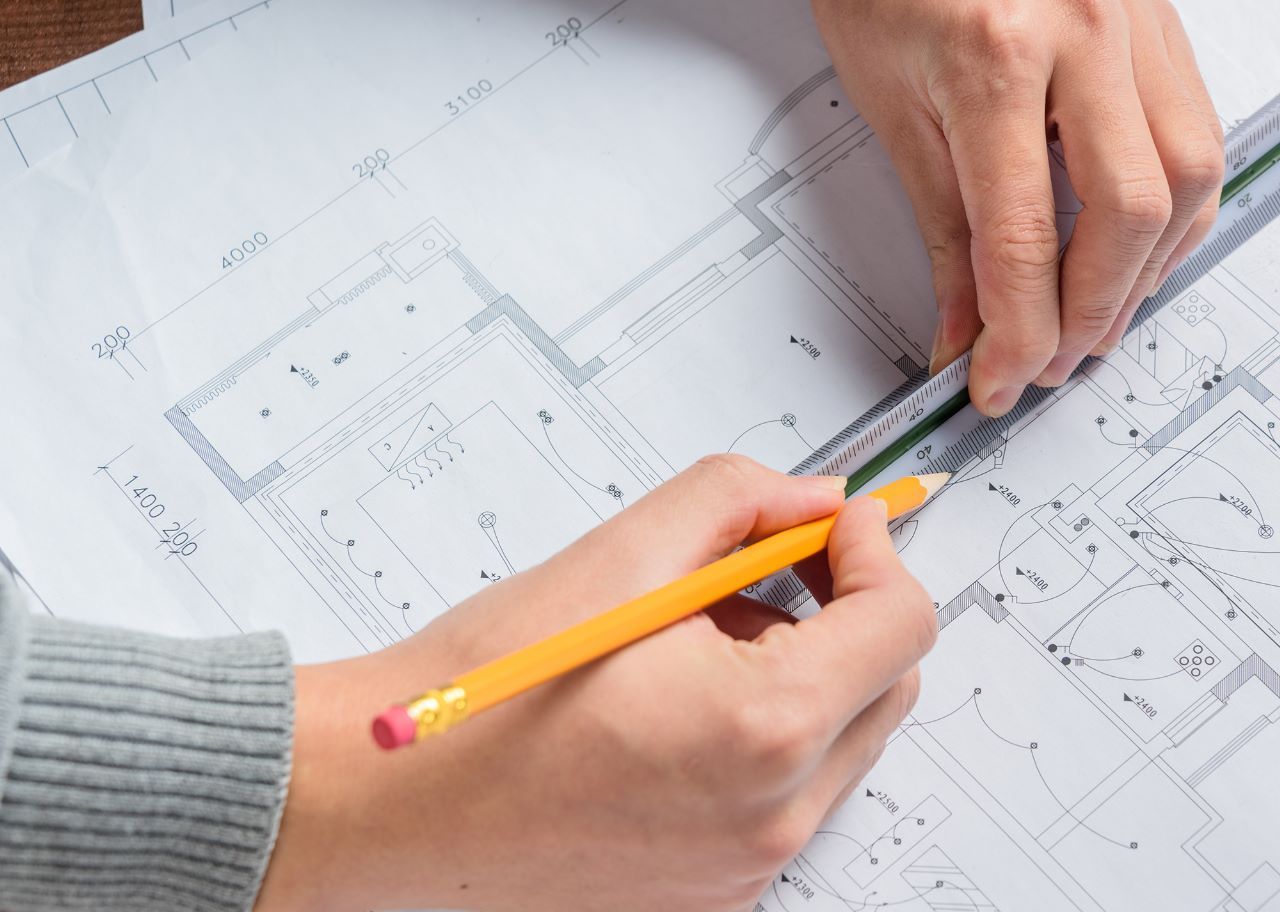 pessoa-calculando-projeto-de-arquitetura Uma pessoa está desenhando uma planta com um lápis.