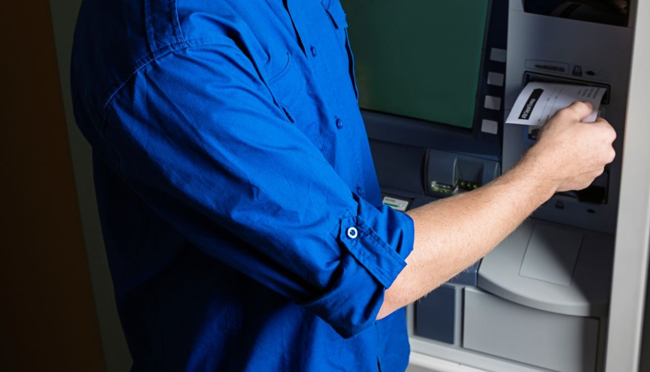 pessoa-no-caixa-eletronico Um homem de camisa azul está usando um caixa eletrônico.