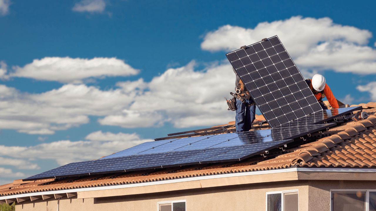 plascas-solares Um homem está instalando painéis solares no telhado de uma casa.