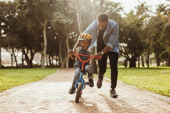 Um homem está ensinando um menino a andar de bicicleta em um parque.