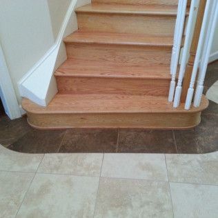 Wooden staircase with a rounded bottom step and white banister in a tiled hallway