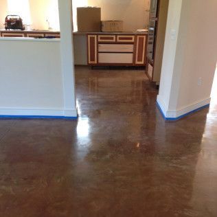 Empty room with glossy brown floor, white walls, and a kitchen visible in the background