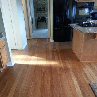 Empty kitchen with hardwood floors, black refrigerator, and sunlight streaming across the room