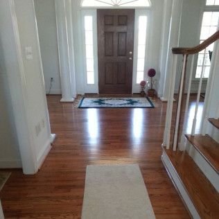 Bright entryway with hardwood floors, a dark front door, white curtains, and a staircase railing on the right