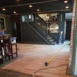 Empty indoor space with dark staircase, wooden floor, and a broom on the floor