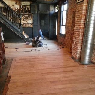 Loft interior with exposed brick, wood floor, staircase, and floor sander near windows