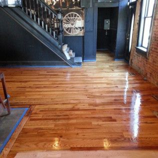 Empty room with polished hardwood floors, dark staircase, and brick walls by large windows