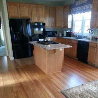 Bright kitchen with black appliances, wood cabinets, granite island, and hardwood floors