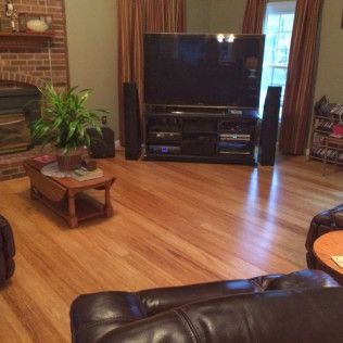 Living room with hardwood floors, TV, coffee table, plants, and brown leather sofa