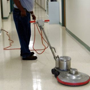 Person using a floor buffer on a shiny hallway floor, with an orange power cord trailing behind.