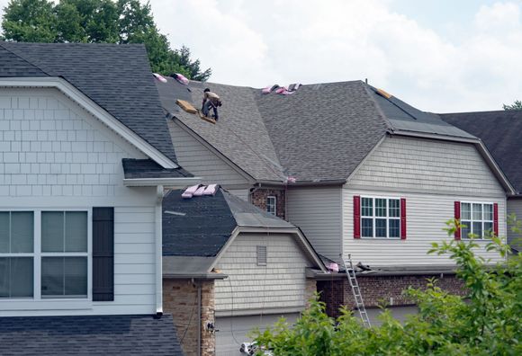Workers repairing a gray roof on a house with ladders and scattered shingles