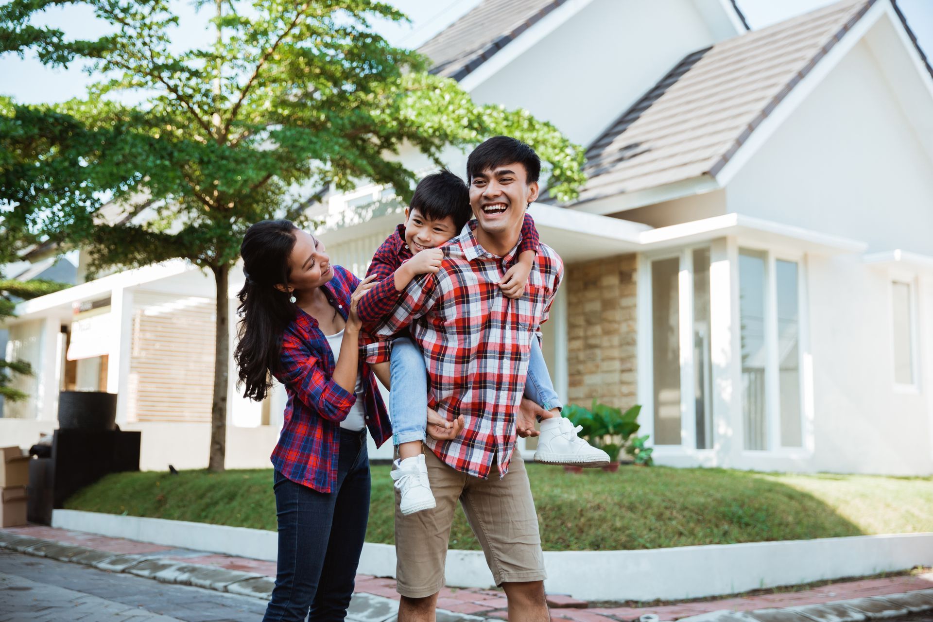 Family smiling outside a white suburban house, with a child on a parent’s back