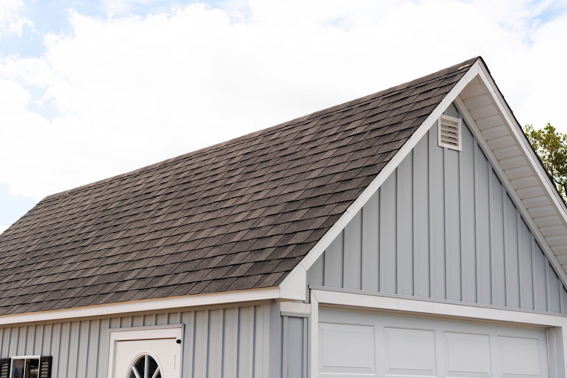 Gray house roof and gable above a white garage door under a cloudy sky