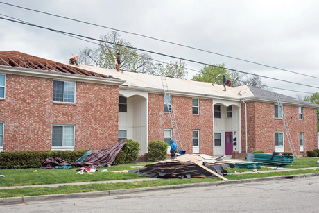 Roofers working on a house roof with green underlayment and scattered tools in a suburban neighborhood