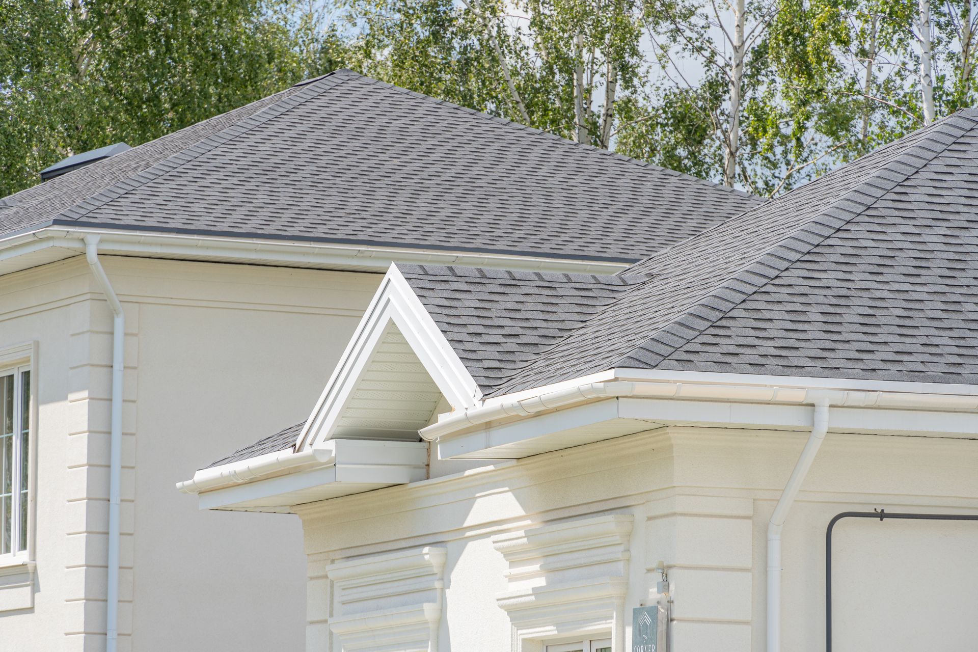 White house roof with gray shingles and a small gabled dormer under trees