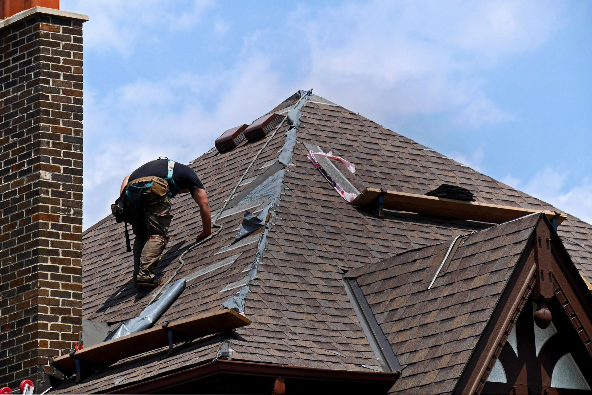 Roofers working on a house roof with green underlayment and scattered tools in a suburban neighborhood