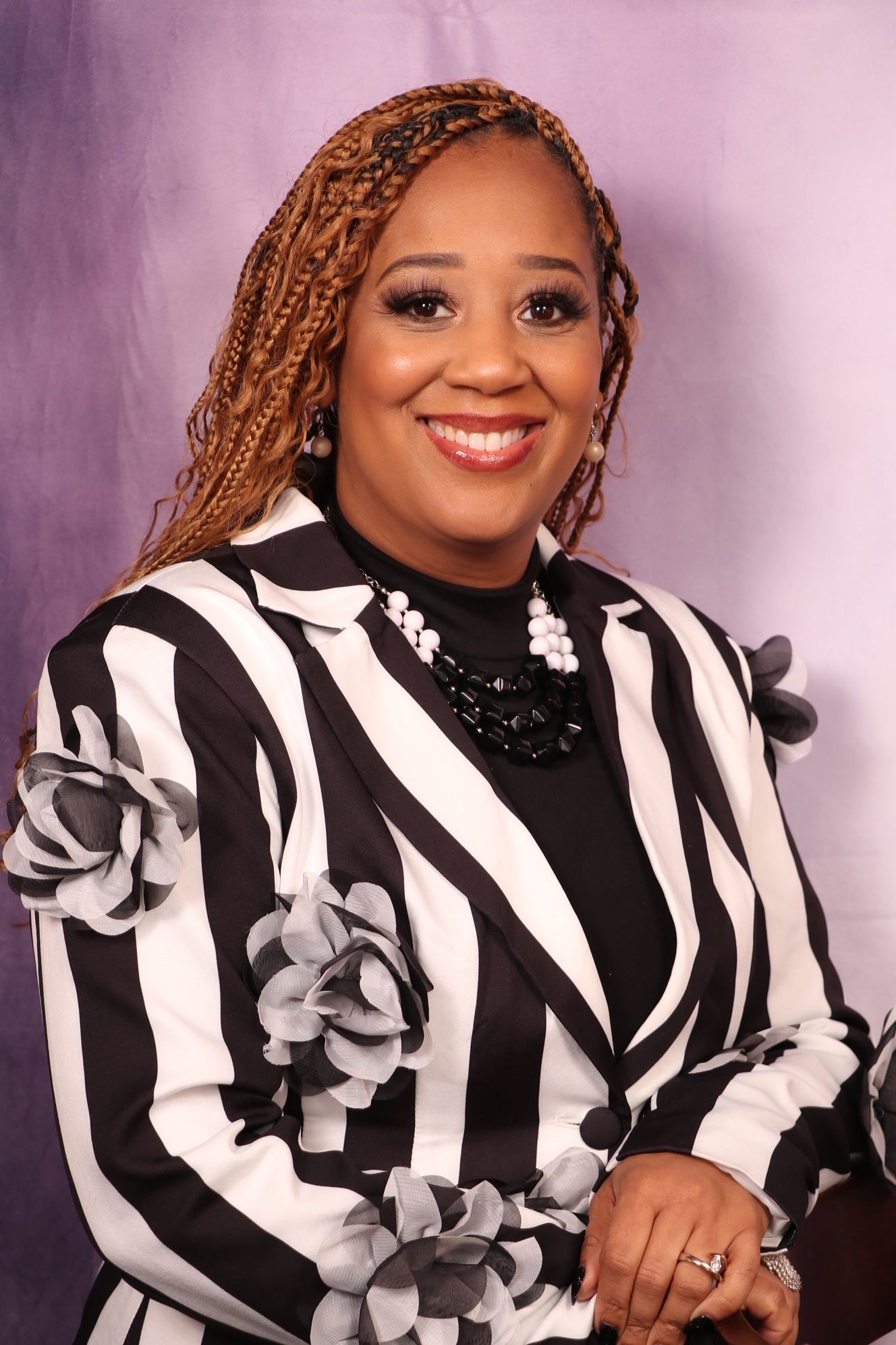Portrait of a smiling woman with braided hair wearing a black-and-white striped jacket with floral accents.