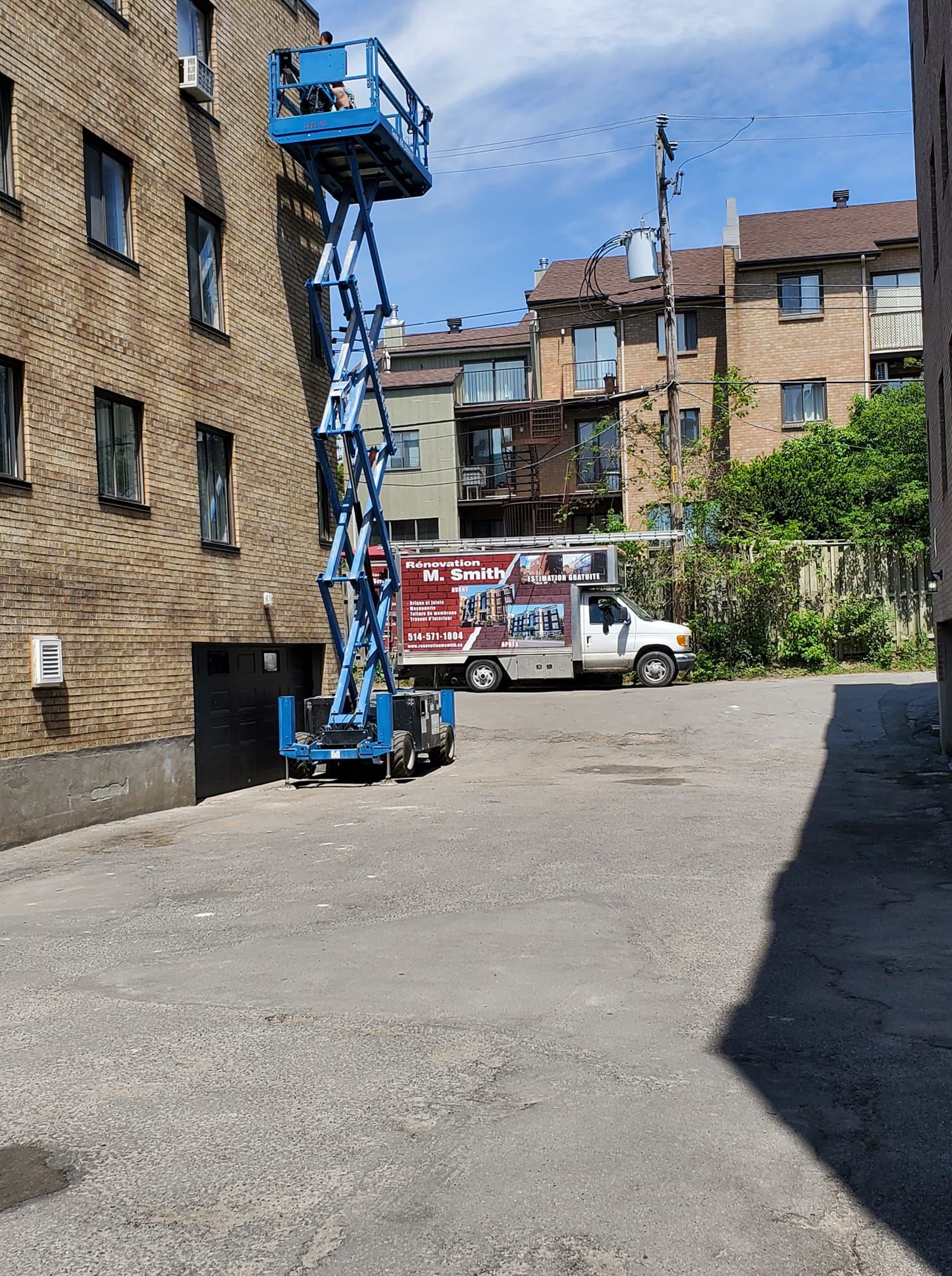 Un ascenseur à ciseaux bleu est garé devant un bâtiment en brique.